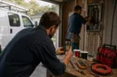 A phone on a small tripod filming an electrician at work, in a natural documentary style.