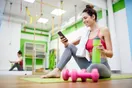 A trainer filming a member doing a lift on a phone mounted on a tripod in a gym, in a natural documentary style.