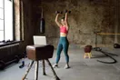 A gym trainer filming a workout demonstration with a phone on a tripod and a ring light, in a natural documentary style.
