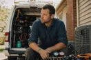An HVAC technician installing a yard sign at the curb of a finished job, in a natural documentary style.