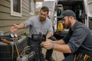 A phone tripod set up while an HVAC technician demonstrates equipment, in a natural documentary style.