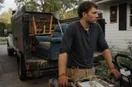 A junk removal operator installing a yard sign at the curb of a finished job, in a natural documentary style.