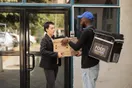 A courier handing a package to a pharmacy receptionist at a front desk, photographed in a natural documentary style.