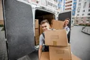A moving company crew and wrapped truck parked outside a suburban home on moving day, natural documentary style.