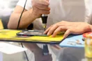 A phone repair storefront with an open sign, a technician visible at the counter helping a walk-in customer, documentary style.