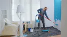 A painter photographing a freshly repainted living room wall on a phone, in a natural documentary style.