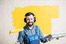 A painter spraying an even coat onto a cabinet door while a phone records the pass, in a plain documentary style.