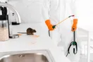 A pest control technician photographed mid-treatment for a social media ad, spraying along a home's foundation, in a natural documentary style.