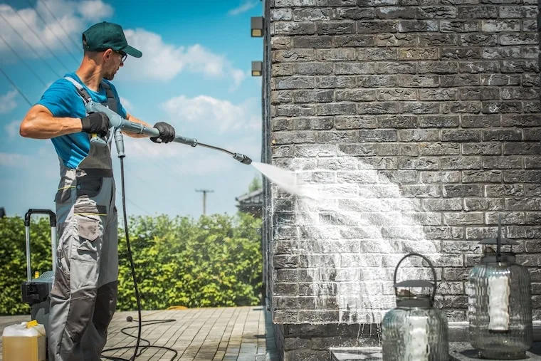 A close-up phone shot of a surface cleaner attachment stripping grime off a patio, with a phone mounted nearby recording, in a natural documentary style.