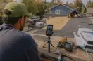 A phone on a small tripod filming a roofing contractor at work, in a natural documentary style.