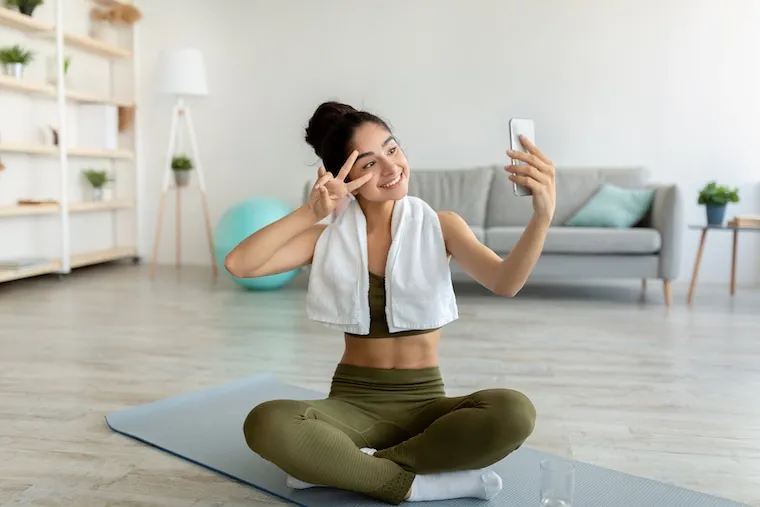 A yoga instructor filming a class clip on a phone tripod in a bright studio, in a natural documentary style.