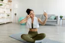 A yoga instructor filming a class clip on a phone tripod in a bright studio, in a natural documentary style.