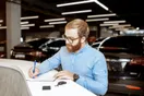 A dealer reviewing license and bond paperwork at a lot office desk with a laptop, in a natural documentary style.