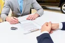 A car rental owner reviewing LLC and insurance paperwork at a desk with a laptop and vehicle titles, natural documentary style.