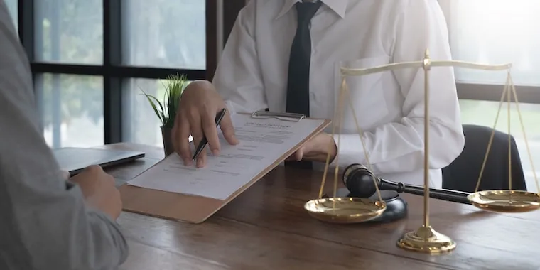 An attorney signing formation documents beside a laptop and a bar-association certificate, in a natural documentary style.