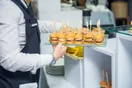 A catering team plating dishes on a stainless steel prep line at an event, in a natural documentary style.