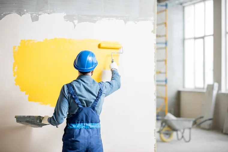 A painter photographing a freshly finished interior wall with a phone for social media, in a natural documentary style.