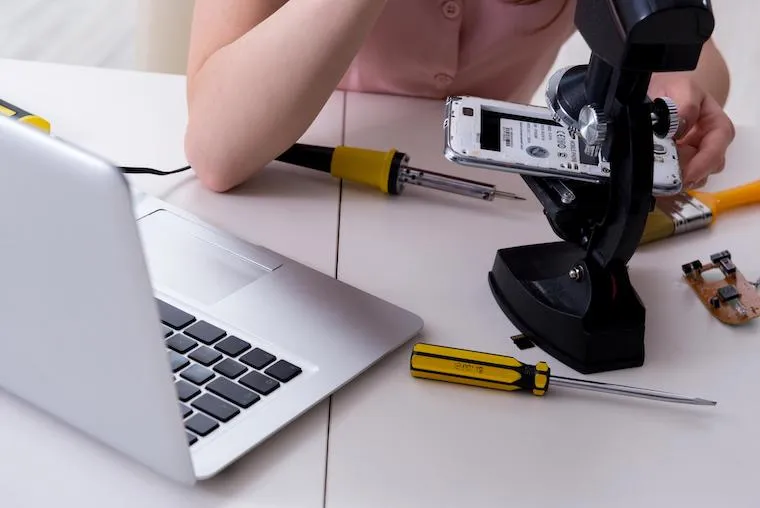 A phone repair technician replying to customer messages on a laptop at the shop counter, in a natural documentary style.