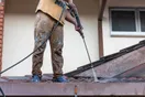 A pressure washing contractor holding a phone showing a Facebook business page with before-and-after photos, standing next to a work van, documentary style.