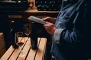 A winery owner filming a phone video among oak barrels in a cellar, shot in a natural documentary style.