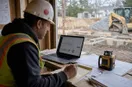 A site contractor reviewing an ad dashboard on a laptop at a workbench, in a natural documentary style.