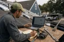 A roofing contractor reviewing an ad dashboard on a laptop at a workbench, in a natural documentary style.