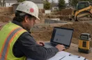 A site contractor studying an ads dashboard with charts on a laptop, in a natural documentary style.