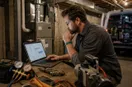 An HVAC technician studying an ads dashboard with charts on a laptop, in a natural documentary style.