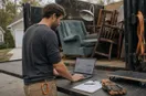 A junk removal operator studying an ads dashboard with charts on a laptop, in a natural documentary style.