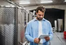 A couple walking through rows of grapevines toward a winery event pavilion at golden hour, in a documentary style.