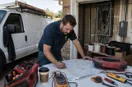 An electrician marking up a paper city map on the hood of a truck, in a natural documentary style.