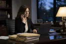 A solo attorney at her desk after hours, phone in one hand and a laptop open to an unanswered email thread, case files stacked beside her.