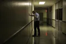 A person stands in a dim courthouse hallway holding a phone to their ear with the other hand pressed against a wall, photographed in a natural documentary style.