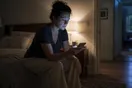 A woman sits on the edge of her bed late at night, phone lit in the dark, waiting for an attorney's website to load.