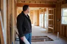 A general contractor stands at a framed-out kitchen remodel site holding blueprints in the early morning light, natural documentary style.