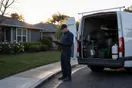A pest control technician checks a clipboard beside his service van outside a suburban home at dawn, sprayer equipment visible in the open van doors, natural documentary style.