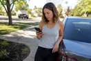 A woman in a driveway checking a car wash website on her phone after a neighbor recommended the unlimited plan, natural documentary style.