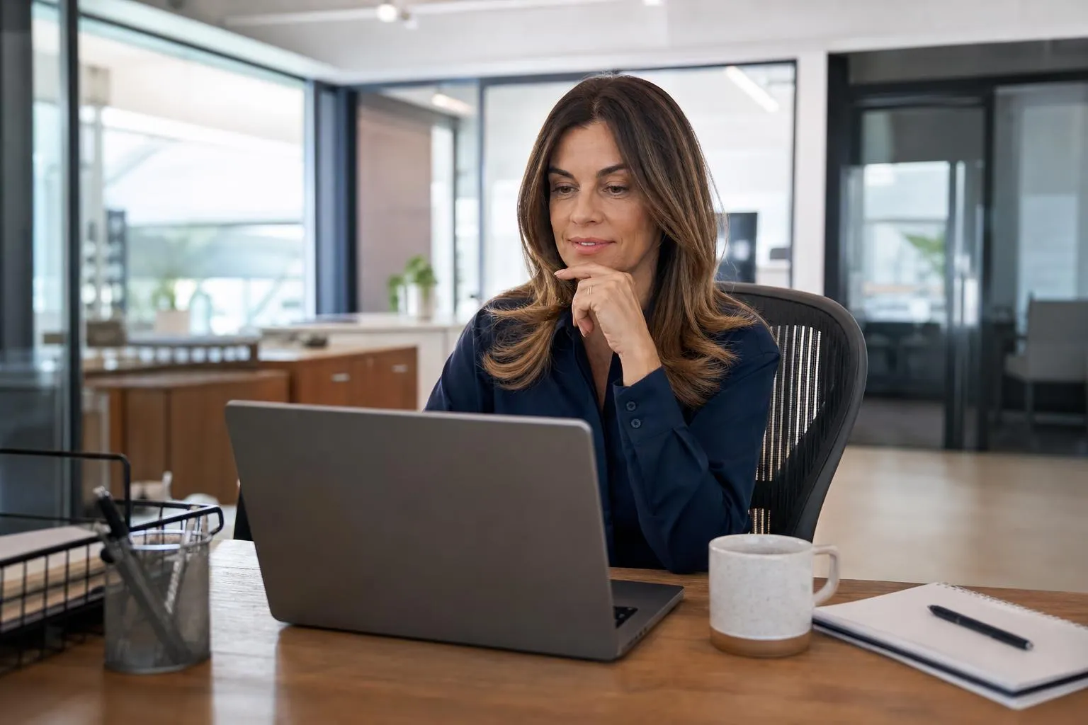 An office manager checking a caterer's website on her laptop during a lunch break, phone with a text recommendation visible nearby, natural documentary style.