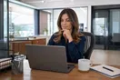 An office manager checking a caterer's website on her laptop during a lunch break, phone with a text recommendation visible nearby, natural documentary style.