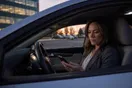 A woman sitting in her parked car outside an office building at dusk, scrolling her phone before dialing a recommended attorney.