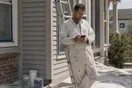 A painter in spattered coveralls leans against a ladder checking a slow-loading website on his phone during a lunch break, in a natural documentary style.