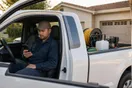 A pest control technician sits in his truck in a driveway checking a quiet phone at the end of a route, in a natural documentary style.