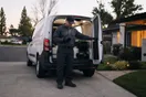 A pest control technician closes up his service van in a suburban driveway at dusk, glancing at his phone before heading home.