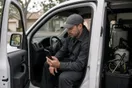 A pest control technician sits in his van checking a slow-loading website on his phone after spotting a roach call come in, in a natural documentary style.