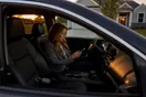 A real estate agent sitting in her parked car outside a listing at dusk, scrolling her phone with a lockbox key in hand.