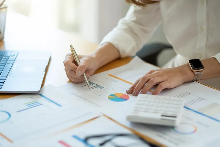 An accountant preparing a client invoice on a laptop with pricing packages printed on the desk, in a natural documentary style.