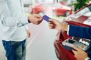 A car rental agent reviewing a rate sheet and payment terminal at a counter with a customer signing a rental agreement, in a natural documentary style.