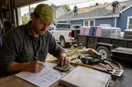 A roofing contractor working out a rate card and a customer invoice at a workbench, in a natural documentary style.