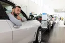 A single used car being inspected on a small lot with a for-sale sign, in a natural documentary style.