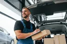 A new delivery business owner loading labeled boxes into a cargo van early in the morning, checklist in hand, documentary style.